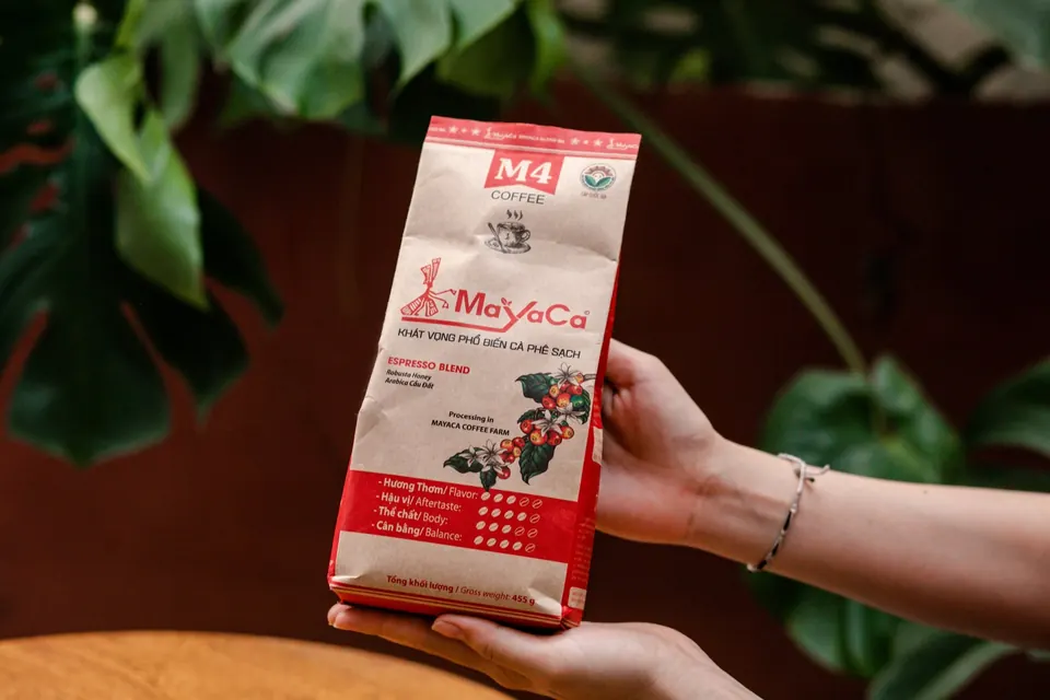 Tay cầm gói cà phê M4 trước nền lá xanh